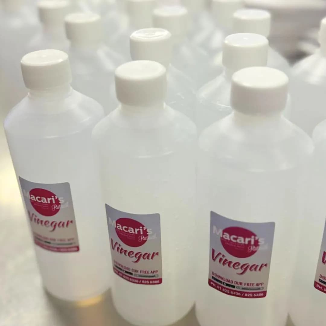 Multiple bottles of Macari’s takeaway vinegar lined up on a counter, filled with clear vinegar and labelled with Macari’s Ratoath branding.